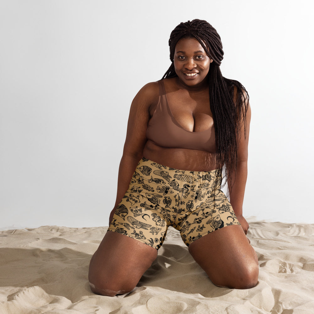 A plus size woman kneeling in sand wearing the Plenty of Fish in The Sea shorts
