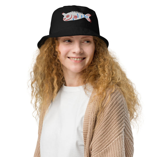 A woman wearing a black bucket hat with a colorful fish embroidery on the front, smiling against a white background.
